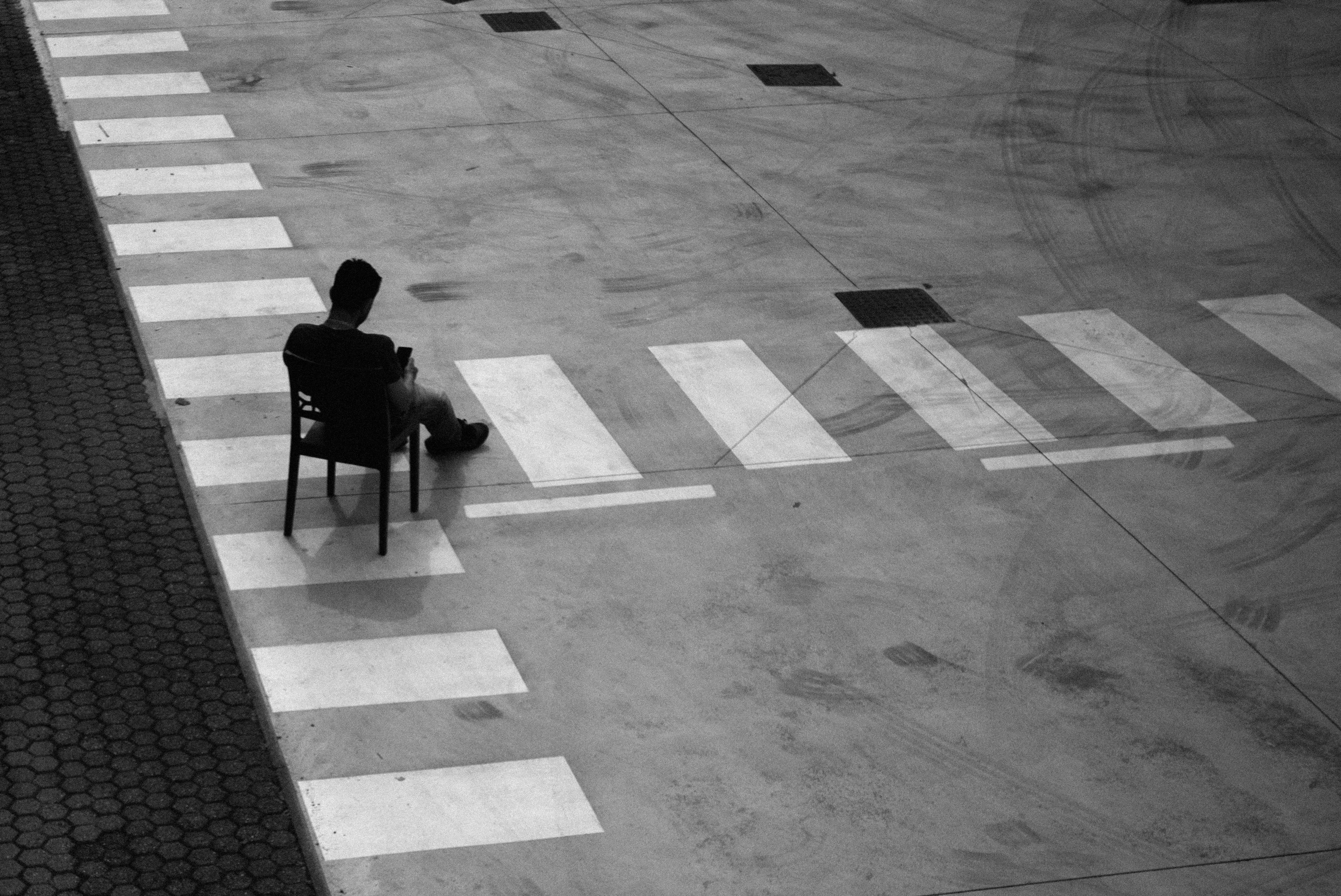 Uomo seduto su una sedia in un parcheggio vuoto, bianco e nero